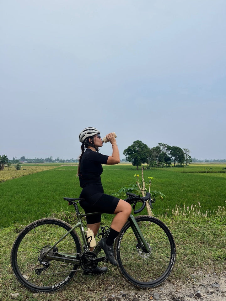 Pesepeda beristirahat dan minum di samping sepeda dengan custom wheelset Strummer menggunakan rim Strummer GC25, berlatar persawahan. Foto milik Novia Kosim (@peanutbutterno9).